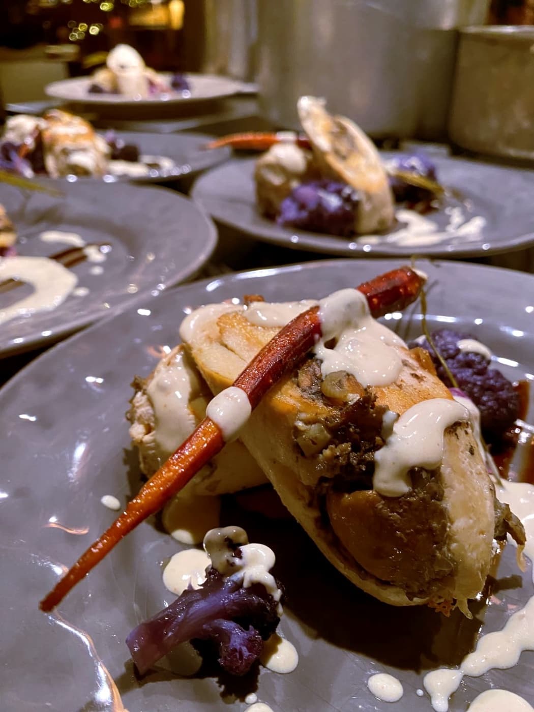 Assiette grise dressée avec une carotte rôtie, une sauce crémeuse et du chou-fleur violet