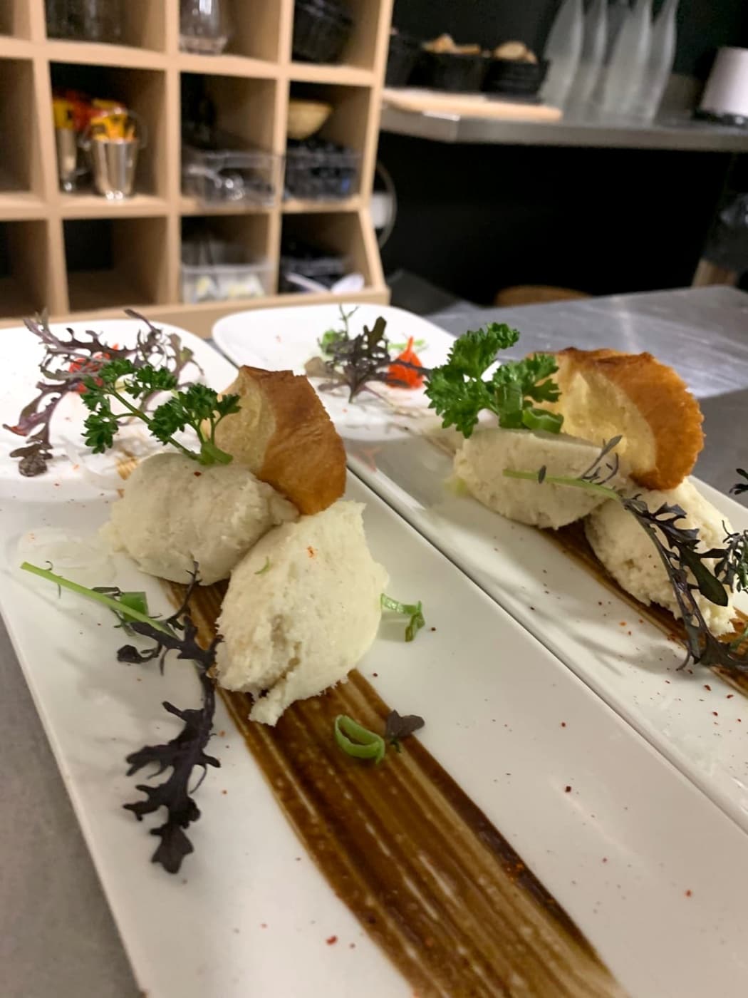 Assiette allongée dressée avec des quenelles, du pain et des herbes