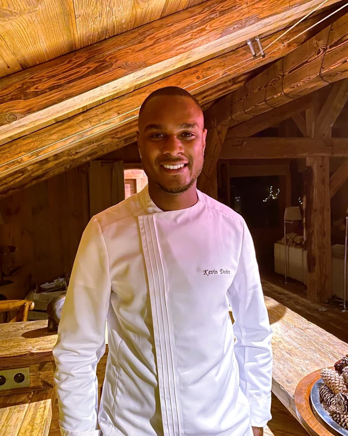Chef Kévin en veste de cuisine blanche, dans un chalet en bois aux lumières chaudes